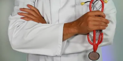 Mainile unui doctor in halat alb incrucisate la piept, cu un stetoscop rosu in mana stanga