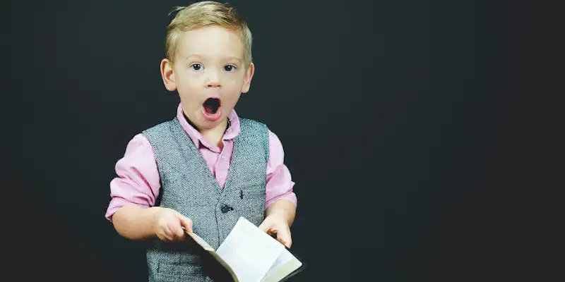 Un baietel cu o carte in mana se minuneaza de ce a citit cu gura larg deschisa si surprindere maxima