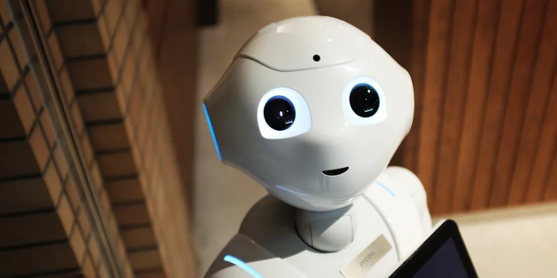 Un robot alb cu ochii mari si o tableta in mana, pe un hol