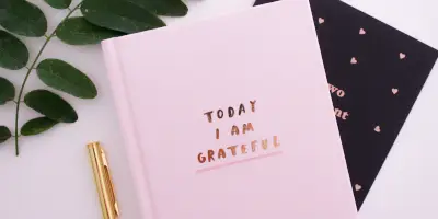 O agenda roz pe care scrie ”today i am grateful”, cu un stilou auriu, pe o masă alba