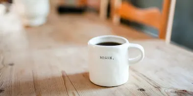 O cana alba mare, plină cu cafea, pe o masa de lemn deschis